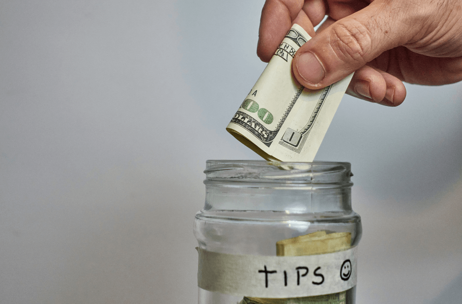 Money being placed in a glass jar marked "Tips"